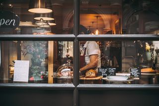 A baker at work behind the cakes, seen through a London café window
